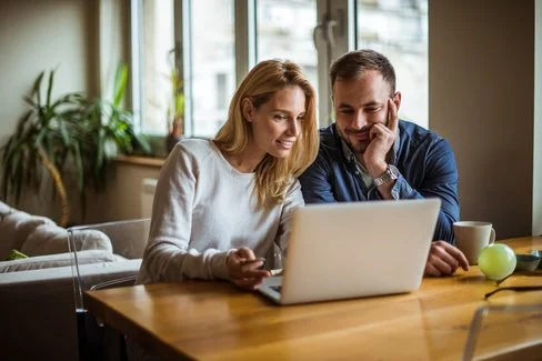 Ein Mann und eine Frau schauen gemeinsam in ihrem Wohnzimmer auf einen Laptop. Die AOK stellt die häufig gestellten Fragen zur AOK.de in den FAQs zusammen.