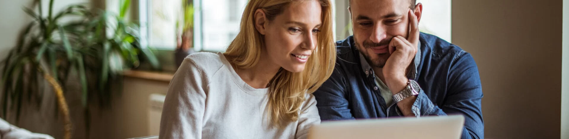 Ein Mann und eine Frau schauen gemeinsam in ihrem Wohnzimmer auf einen Laptop. Die AOK stellt die häufig gestellten Fragen zur AOK.de in den FAQs zusammen.