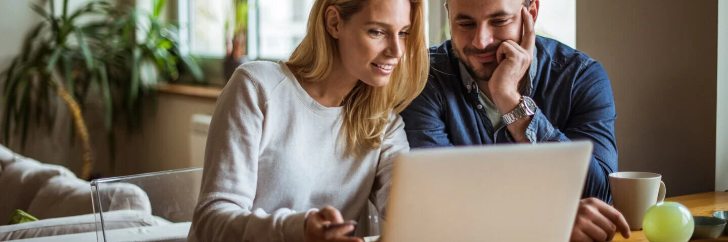 Ein Mann und eine Frau schauen gemeinsam in ihrem Wohnzimmer auf einen Laptop. Die AOK stellt die häufig gestellten Fragen zur AOK.de in den FAQs zusammen.