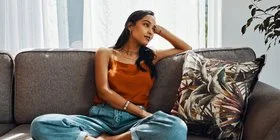 Junge Frau sitzt nachdenklich auf ihrem Sofa.