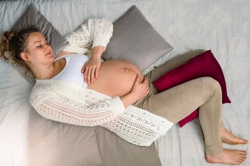 Eine schwangere Frau liegt auf einem Bett und hält ihren Bauch, auf dem eine Linea negra erkennbar ist.