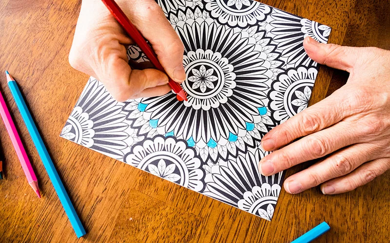 Großaufnahme eines Mandalas, dass von einer Person mit Buntstiften ausgemalt wird.