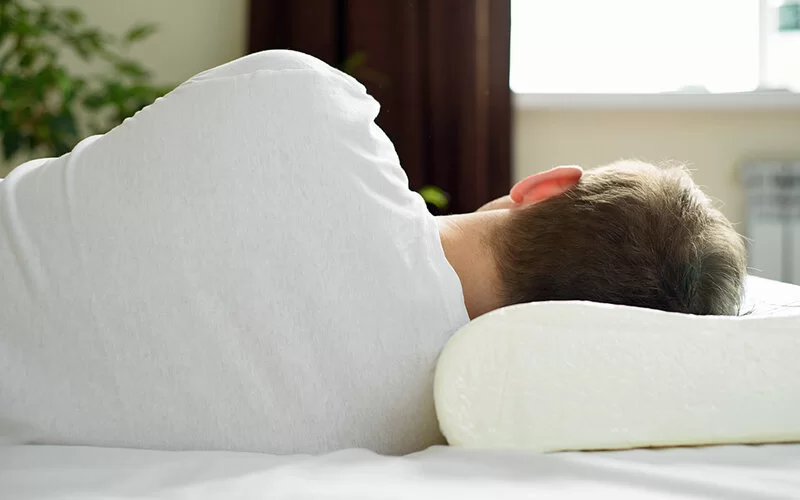 Ein Mann dreht den Rücken zu und schläft auf einem orthopädischen Kopfkissen.