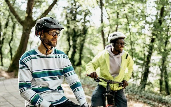 Zwei Männer mit Fahrradhelmen stehen mit ihren Fahrrädern auf einem Waldweg.