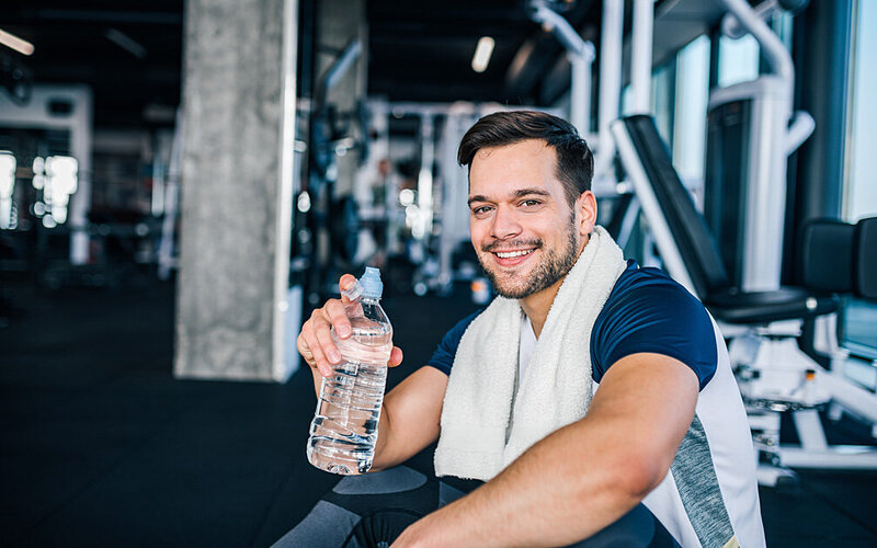Junger Mann macht beim Training eine Ruhepause und trinkt Wasser, um Übelkeit nach dem Sport zu vermeiden.