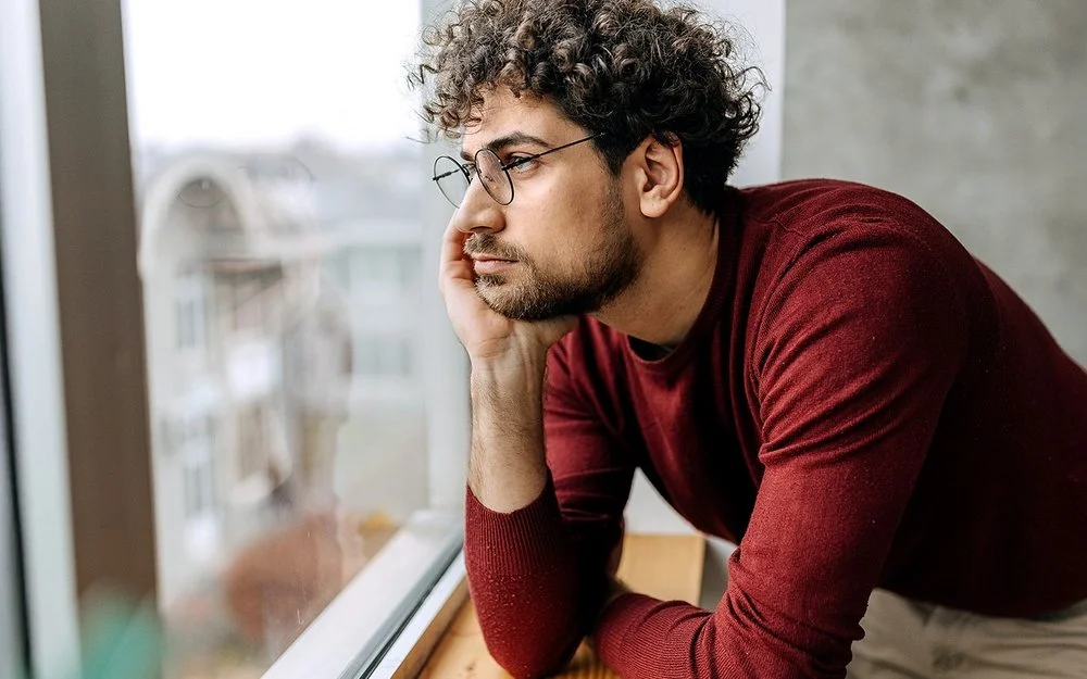 Ein Mann hat den Kopf in die Hand gestützt und schaut aus dem Fenster.