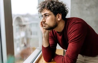 Ein Mann hat den Kopf in die Hand gestützt und schaut aus dem Fenster.