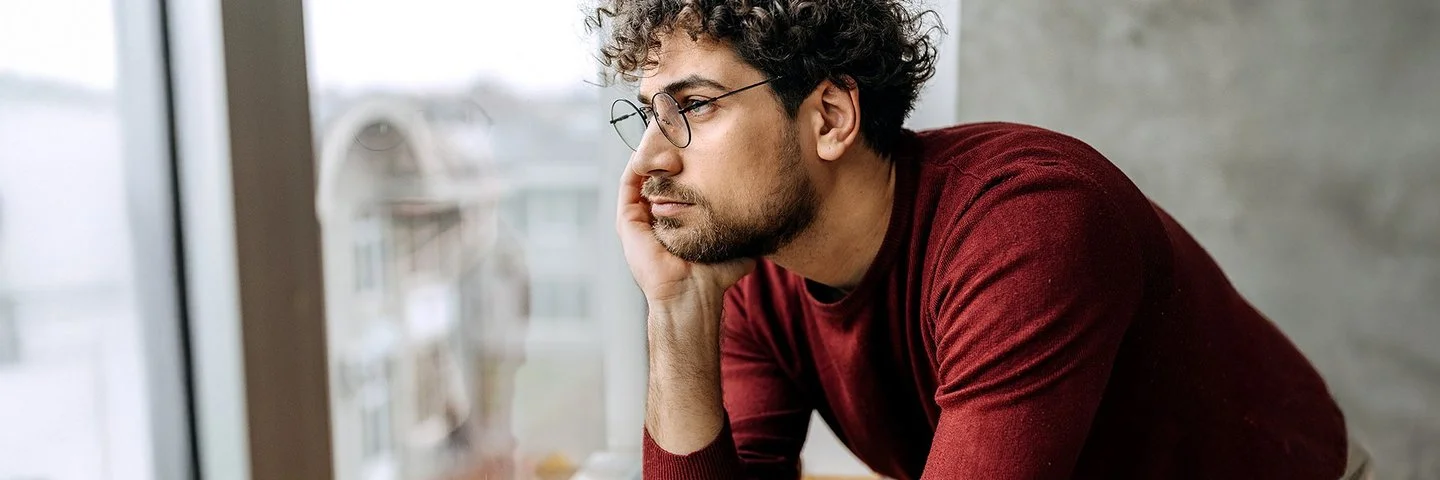 Ein Mann hat den Kopf in die Hand gestützt und schaut aus dem Fenster.