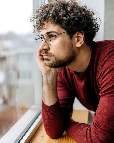 Ein Mann hat den Kopf in die Hand gestützt und schaut aus dem Fenster.