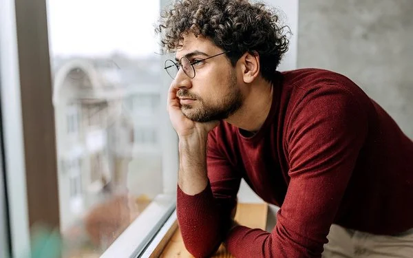 Ein Mann hat den Kopf in die Hand gestützt und schaut aus dem Fenster.