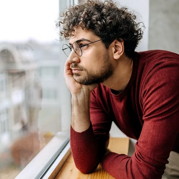 Ein Mann hat den Kopf in die Hand gestützt und schaut aus dem Fenster.