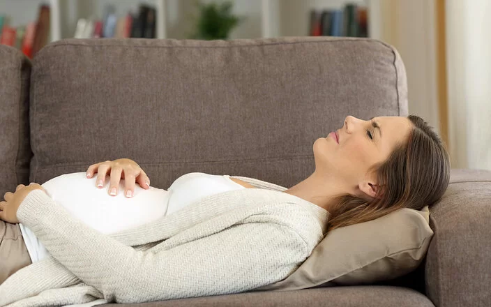 Schwangere Frau hat sich wegen ihrer Symphysenschmerzen auf ein Sofa gelegt.