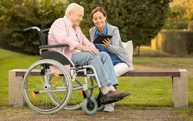 Ein an der Autoimmunerkrankung Multiple Sklerose Erkrankter im Rollstuhl schaut sich zusammen mit seiner Begleiterin im Park etwas auf einem Tablet an.