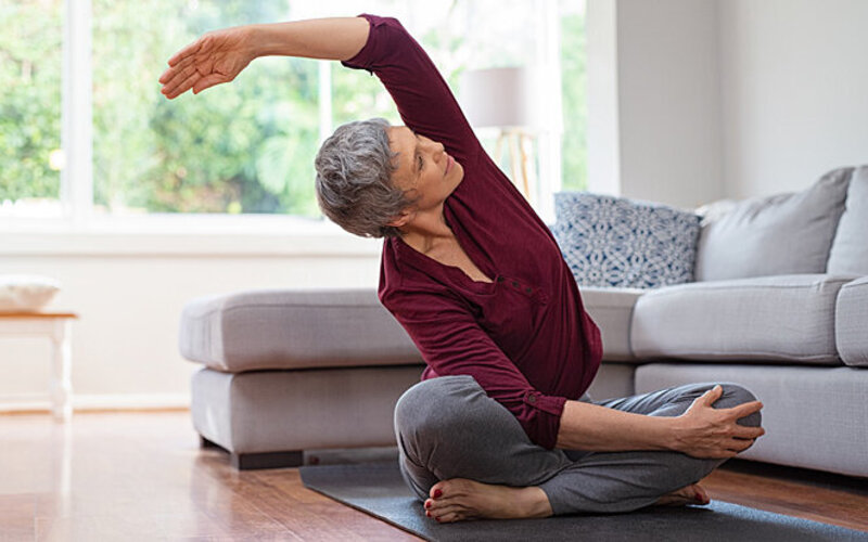 Eine ältere Frau macht Dehnübungen auf einer Yogamatte.