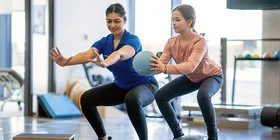 Eine Physiotherapeutin macht mit einem Mädchen Übungen mit einem Ball. Kinder lernen in der Reha, mit Erkrankungen umzugehen.