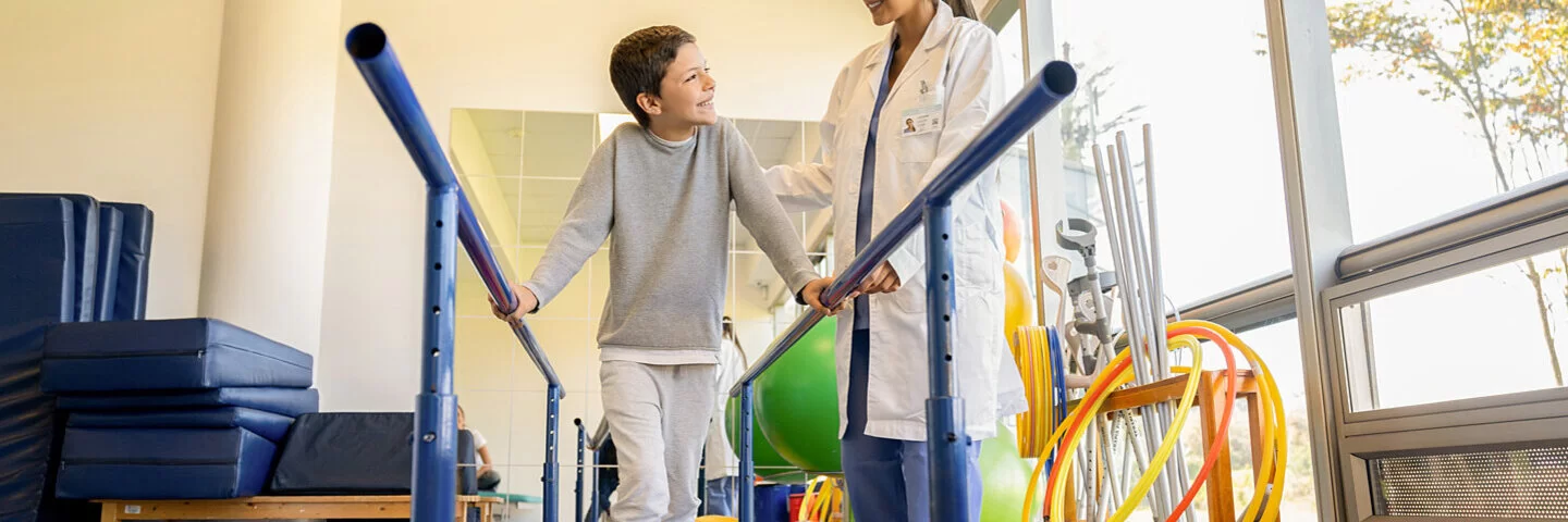 Eine Physiotherapeutin macht mit einem Jungen Gehübungen. Kinder lernen in der Reha, mit Erkrankungen umzugehen.