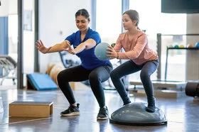 Eine Physiotherapeutin macht mit einem Mädchen Übungen mit einem Ball. Kinder lernen in der Reha, mit Erkrankungen umzugehen.