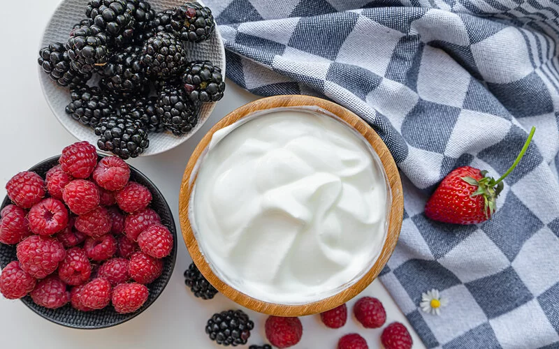 Eine Schale mit Joghurt steht neben zwei Schalen mit frischen Beeren.