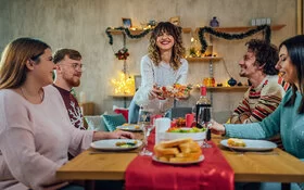 Eine junge Frau serviert ihren vier Freunden und Freundinnen einen vegetarischen Salat an einem geschmückten Tisch.