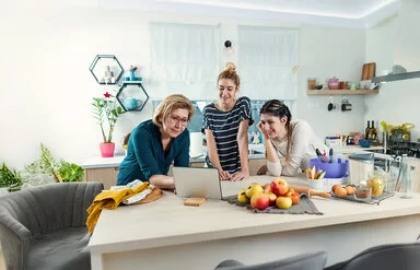 Eine Frau blickt mit zwei Mädchen in ihrer Küche auf den Bildschirm eines Tablets.