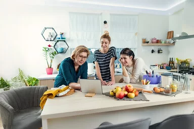 Eine Frau blickt mit zwei Mädchen in ihrer Küche auf den Bildschirm eines Tablets.