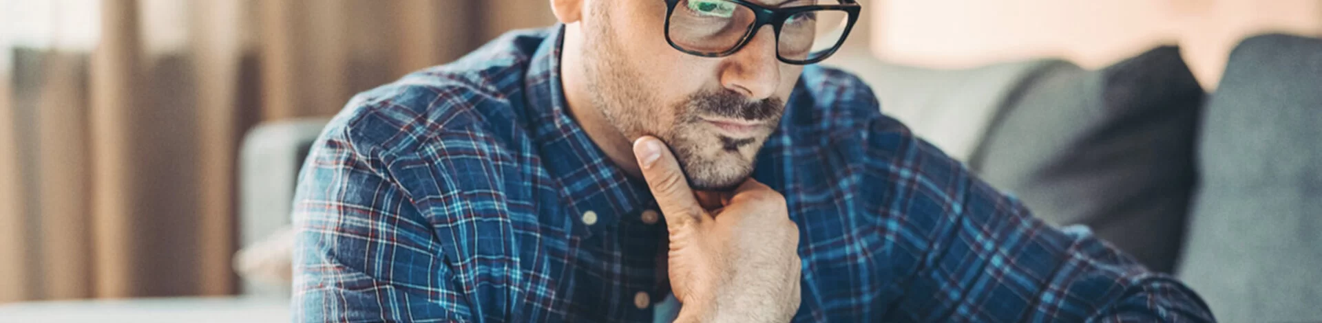 Ein junger Mann mit Brille stüzt das mit der rechten Hand ab und blickt auf den Bildschirm eines Laptops.