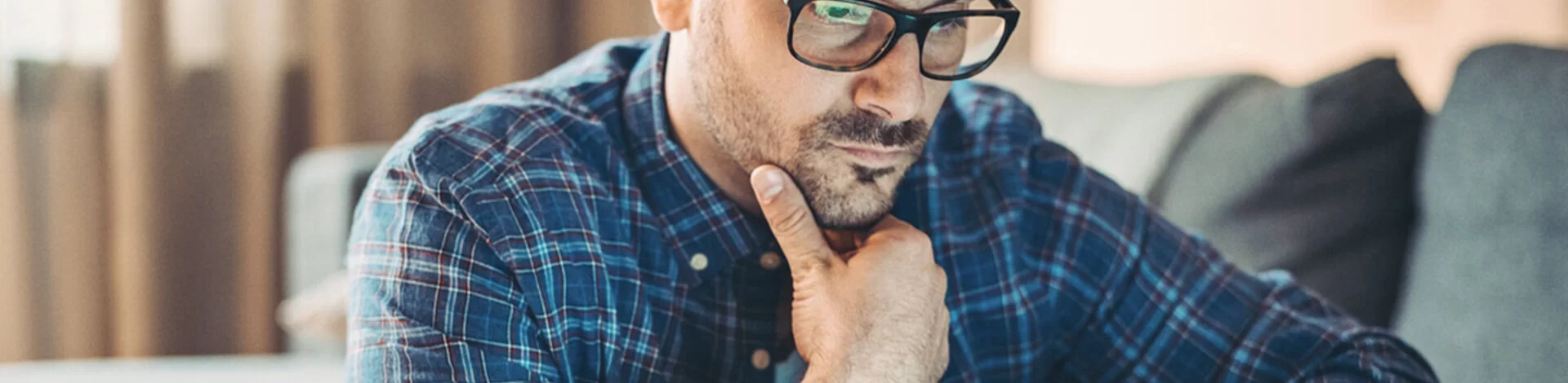 Ein junger Mann mit Brille stüzt das mit der rechten Hand ab und blickt auf den Bildschirm eines Laptops.