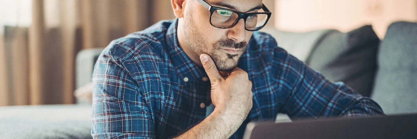 Ein junger Mann mit Brille stüzt das mit der rechten Hand ab und blickt auf den Bildschirm eines Laptops.