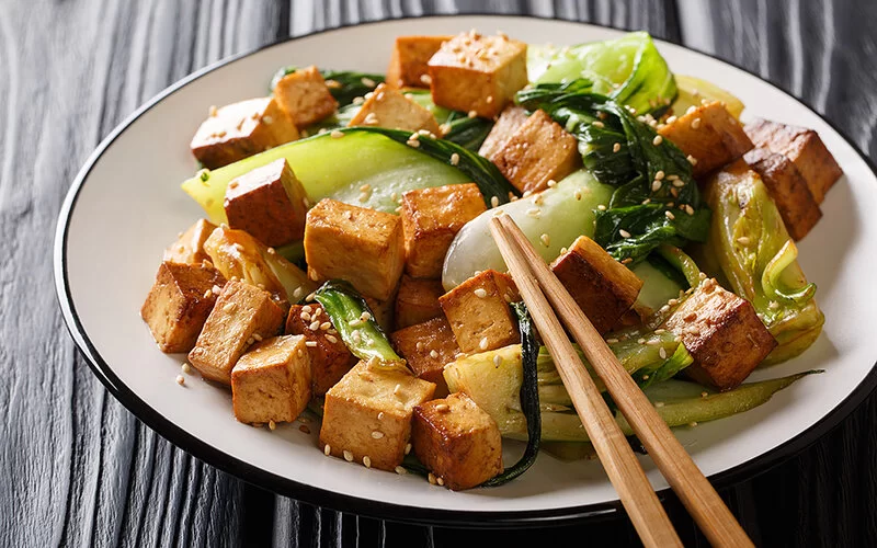 Gebratene Tofu-Stücke und Pak Choi mit Sojasauce und Sesam auf einem Teller.