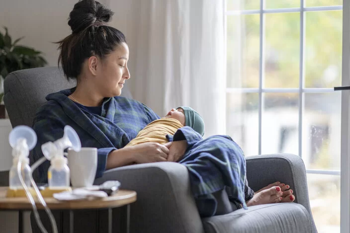 Eine junge Mutter sitzt mit ihrem Baby neben einer Milchpumpe.
