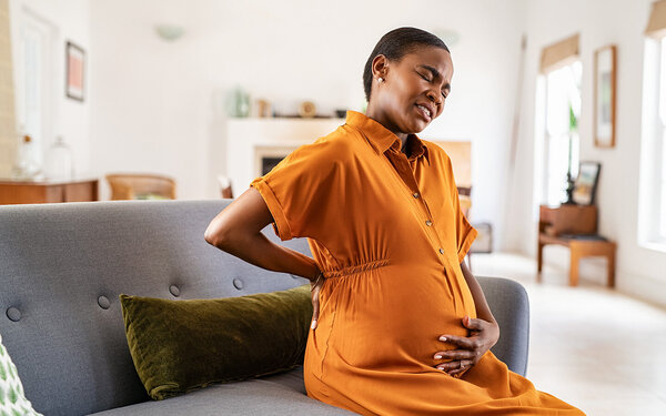 Eine schwangere Frau sitzt auf der Couch und hat Rückenschmerzen.
