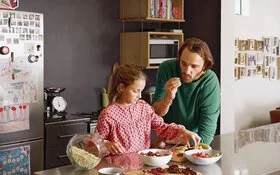 Vater und Tocher essen Obst in der Küche.