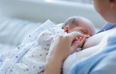 Eine Mutter liegt im Bett und stillt ihr Neugeborenes.