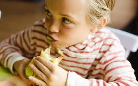 Kind isst Brot mit Gurken, denn eine gesunde Ernährung verhindert Übergewicht.