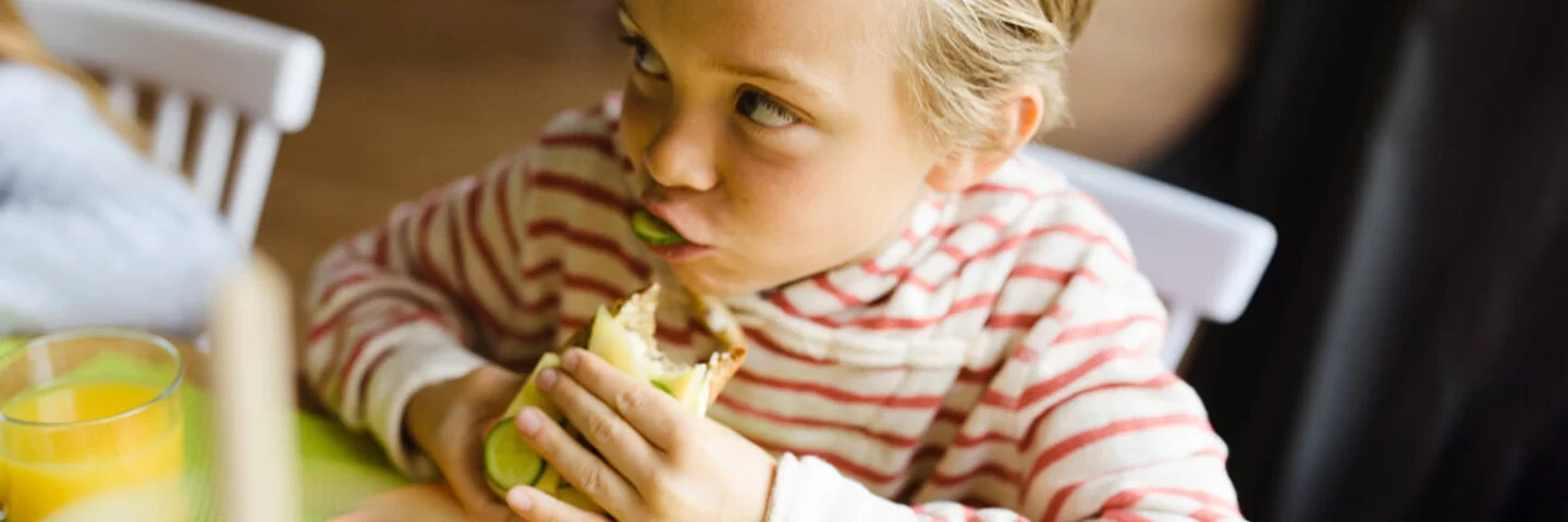Kind isst Brot mit Gurken, denn eine gesunde Ernährung verhindert Übergewicht.
