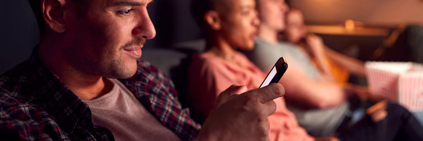 Ein Mann sitzt mit Freunden auf der Couch und checkt sein Smartphone aus Angst, etwas zu verpassen.