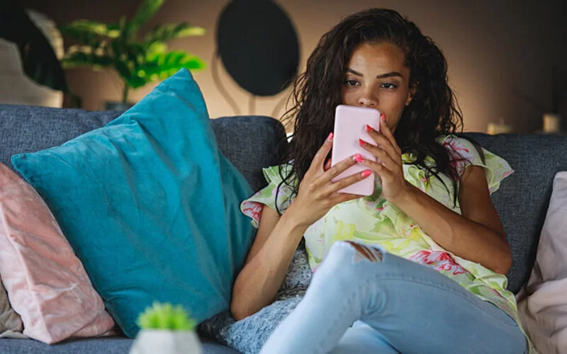 Eine Frau sitzt auf dem Sofa und surft in den sozialen Netzwerken, wo sie mit Toxic Positivity konfrontiert wird.
