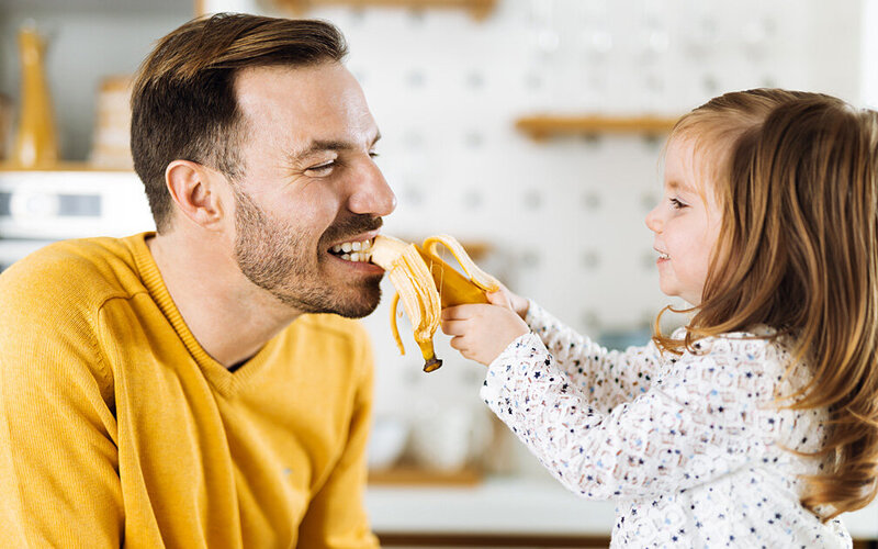 Ein Kind füttert seinen Vater mit einer kaliumreichen Banane.
