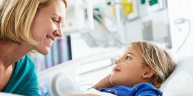 Eine junge Frau beugt sich lächelnd zu einem Kind, das in einem Krankenhausbett liegt.