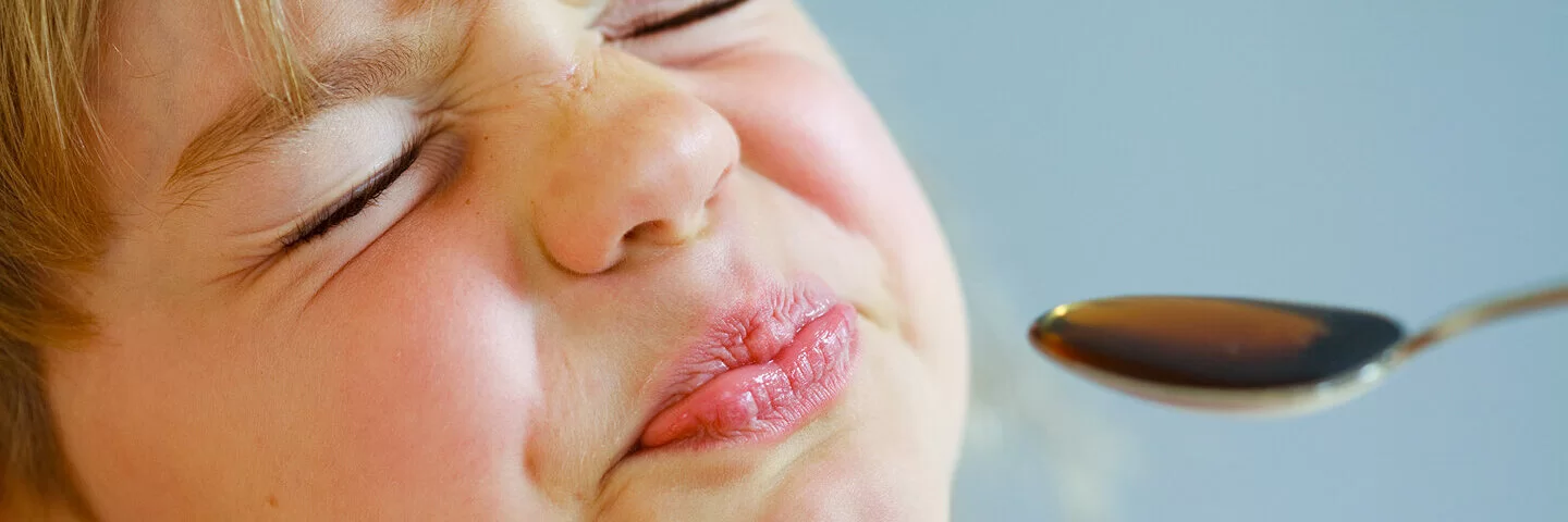 Kleiner Junge bekommt flüssige Medizin mit einem Löffel verabreicht und verzieht das Gesicht.