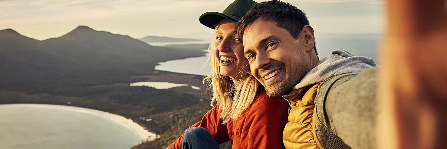 Ein Mann und eine Frau machen ein Selfie mit Bergen und Seen im Hintergrund.