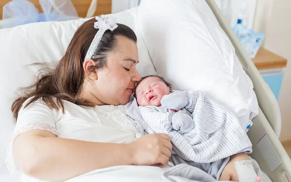 Eine übergewichtige Frau liegt mit einem Baby im Arm in einem Krankenhausbett.