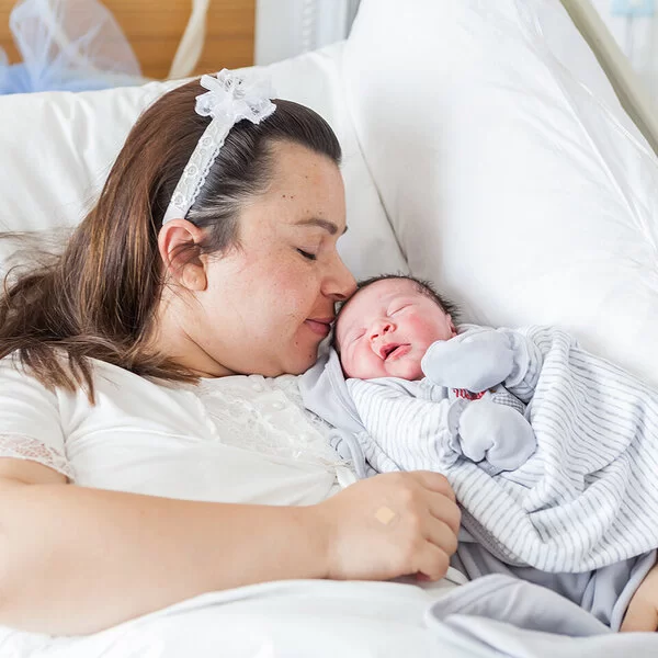 Eine übergewichtige Frau liegt mit einem Baby im Arm in einem Krankenhausbett.