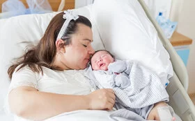 Eine übergewichtige Frau liegt mit einem Baby im Arm in einem Krankenhausbett.