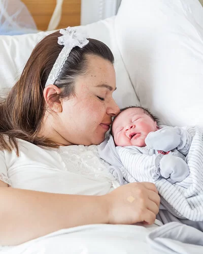 Eine übergewichtige Frau liegt mit einem Baby im Arm in einem Krankenhausbett.