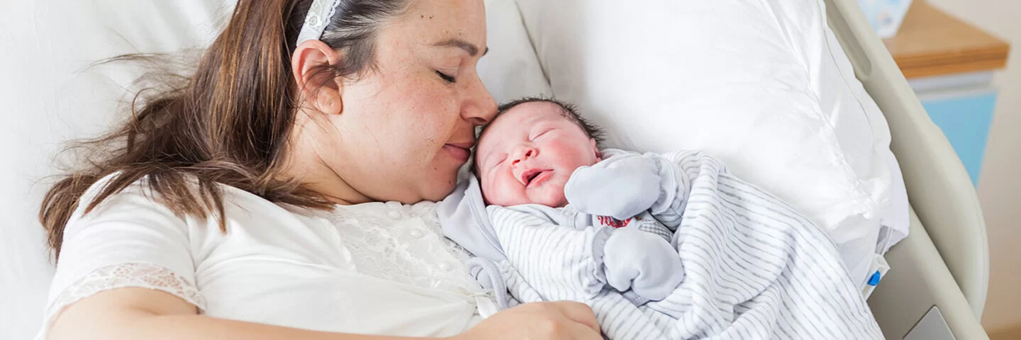 Eine übergewichtige Frau liegt mit einem Baby im Arm in einem Krankenhausbett.