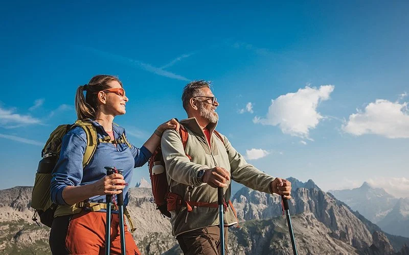 Eine Frau und ein Mann im mittleren Alter wandern mit Rücksäcken und Wanderstöcken in den Alpen.