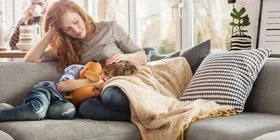 Junge Frau liegt mit erkranktem Kind auf dem Sofa.