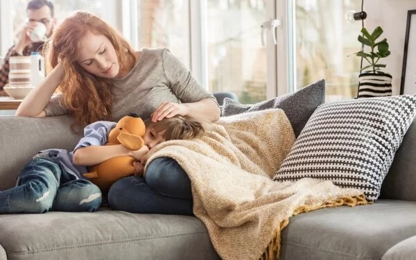 Junge Frau liegt mit erkranktem Kind auf dem Sofa.