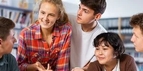 Eine Klassensprecherin, eine weitere Schülerin und drei Schüler unterhalten sich in der Bibliothek angeregt mit ihrer Lehrerin.